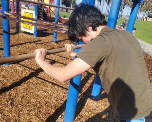 neurodiverse teen practicing bodyweight strength and coordination on outdoor playground bars